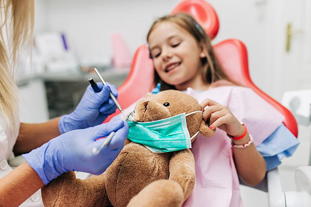 Nettes kleines Mädchen sitzt auf Zahnarztstuhl und hat zahnärztliche Behandlung
