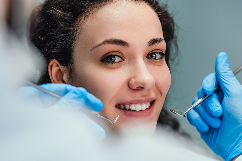Lächelnde Frau sitzt im Zahnarztstuhl und ist bereit für eine zahnärztliche Untersuchung.